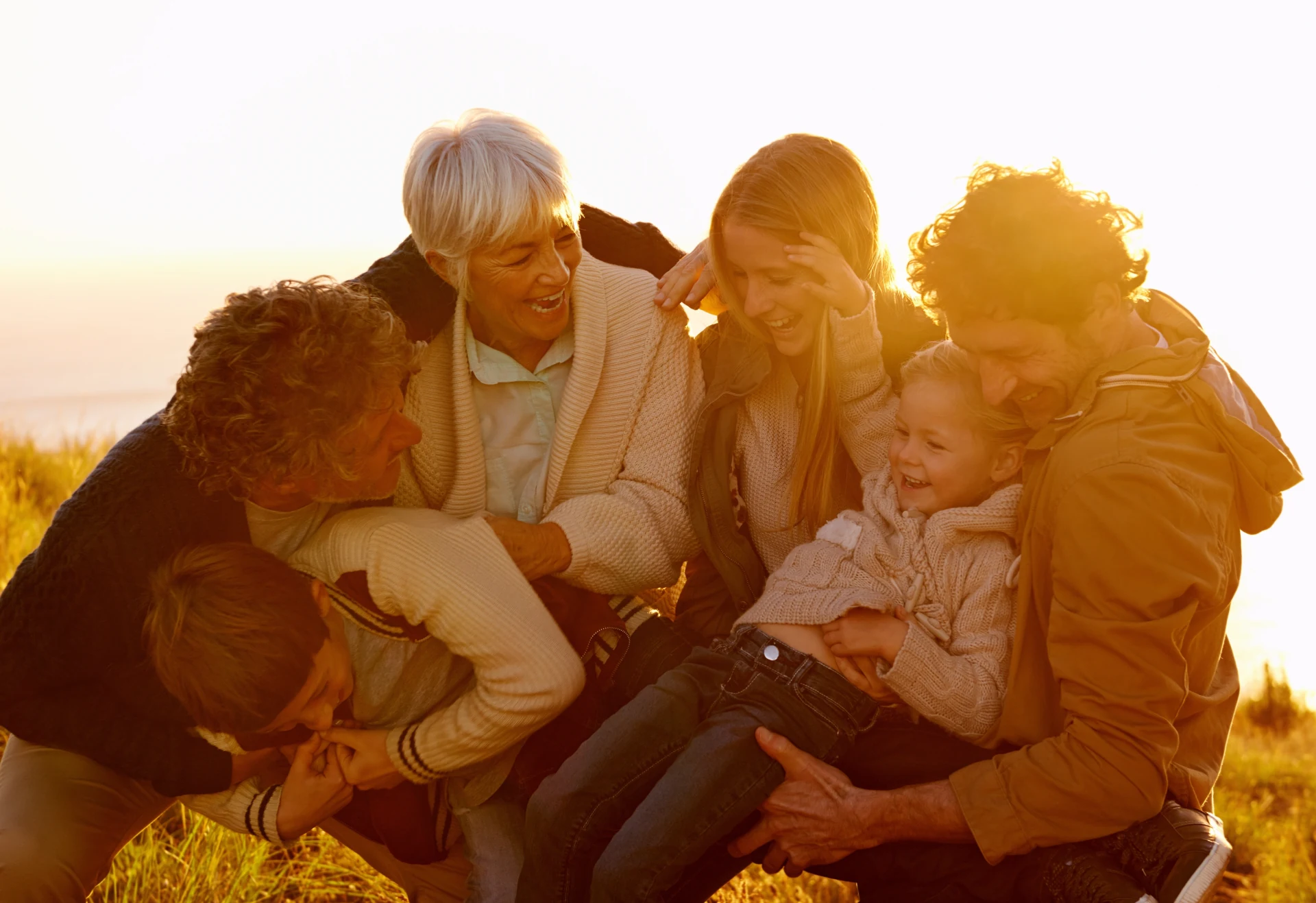 Three generations of a family laughing together outdoors at sunset