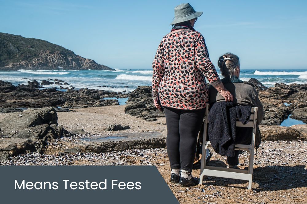 Means Tested Fees Elderly person with adult child sitting on beach