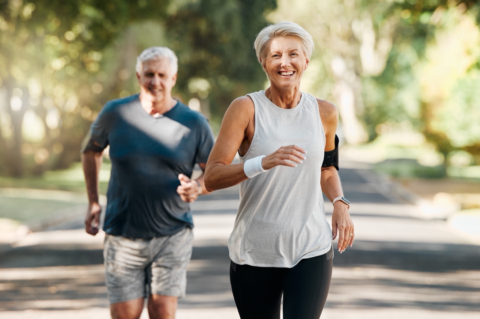 An older couple jogging together along a tree-lined path.