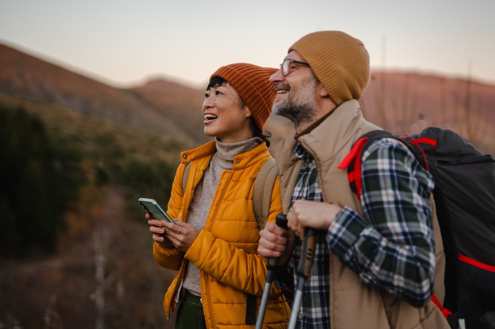 A couple with backpacks and walking poles looking across a mountain landscape.