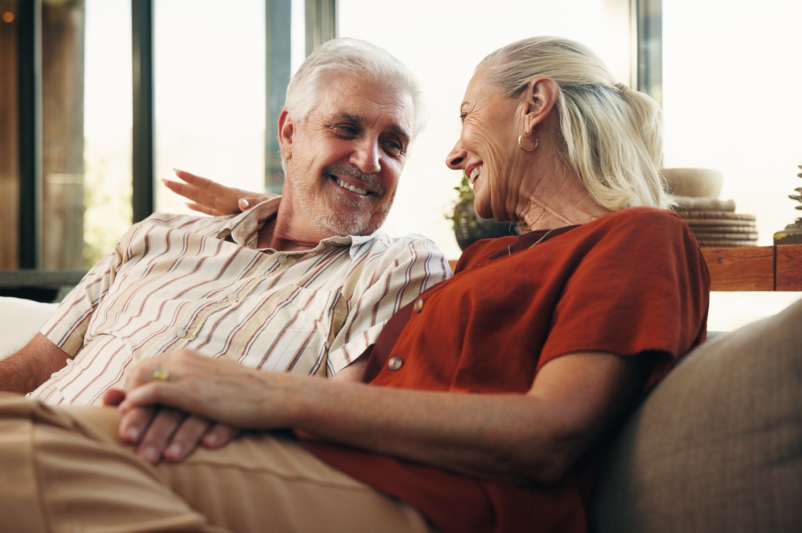 An older couple smiling at each other and holding hands on a sofa.