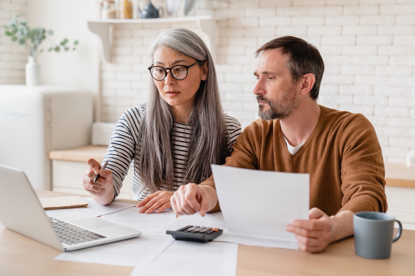 A couple reviewing paperwork beside a laptop and calculator.