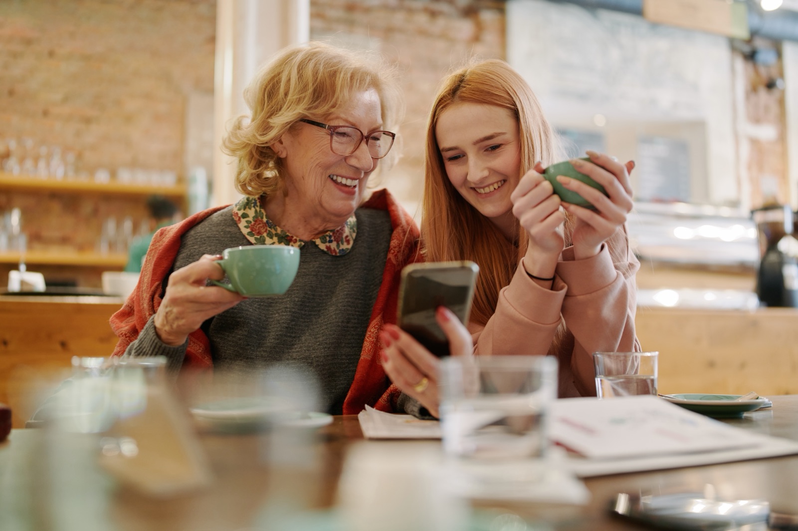 An older woman and a younger woman looking at a smartphone over coffee.