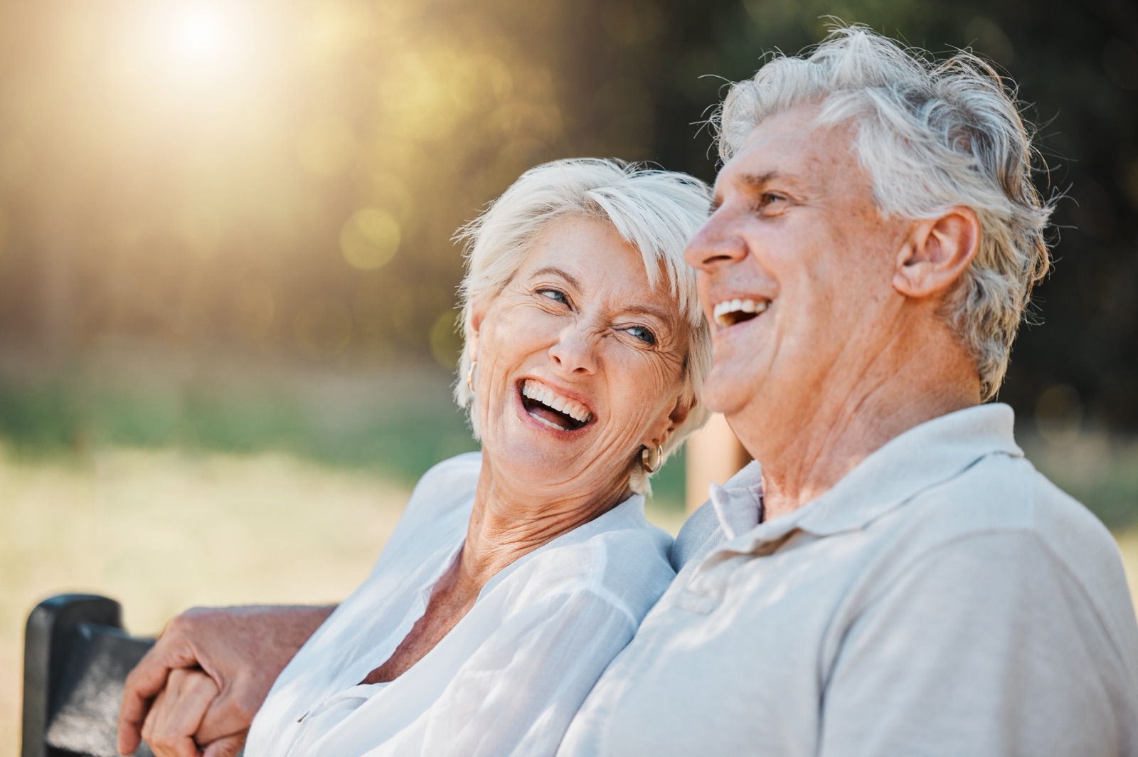 An older couple laughing together on a park bench.