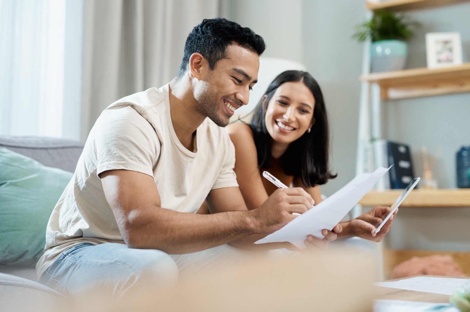 A couple reviewing paperwork and a tablet together on a sofa.