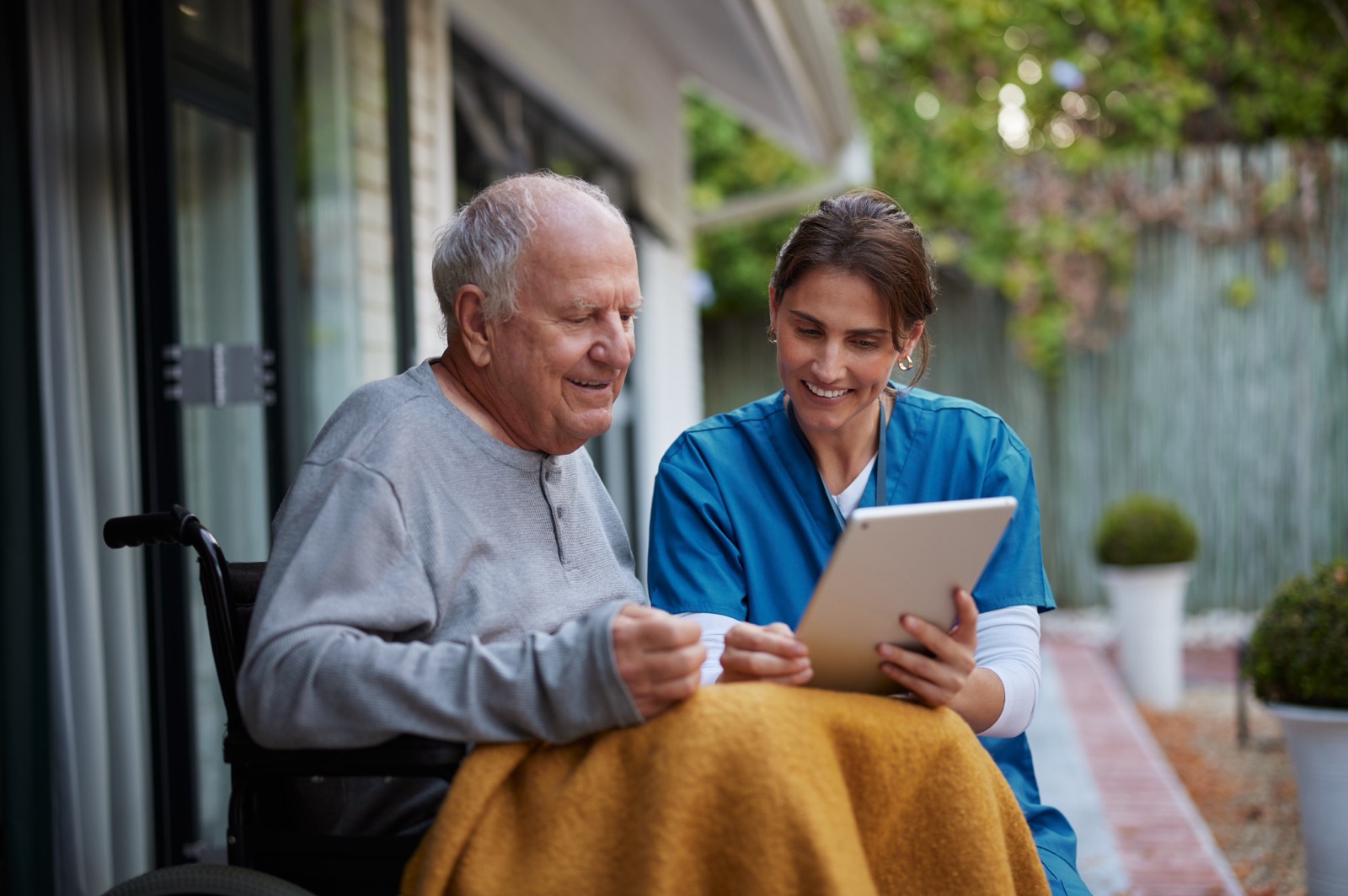 An older man in a wheelchair looking at a tablet with a woman in a blue uniform.
