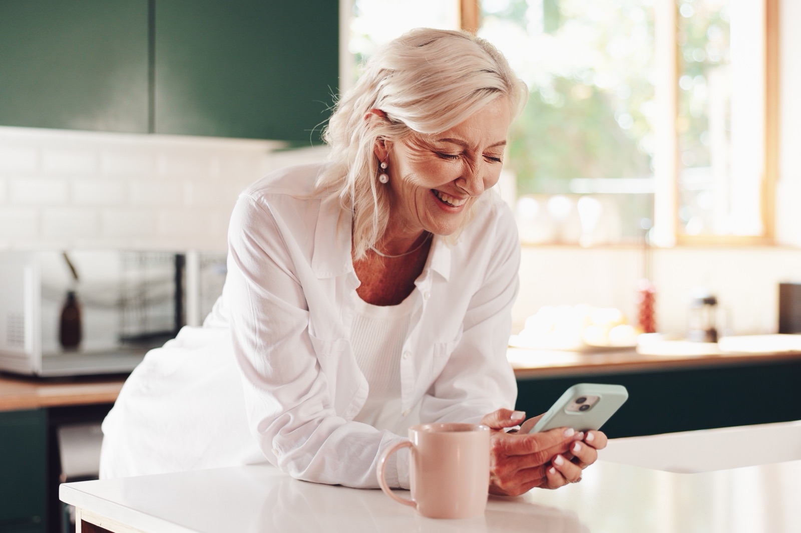 An older woman using a smartphone at a kitchen counter.