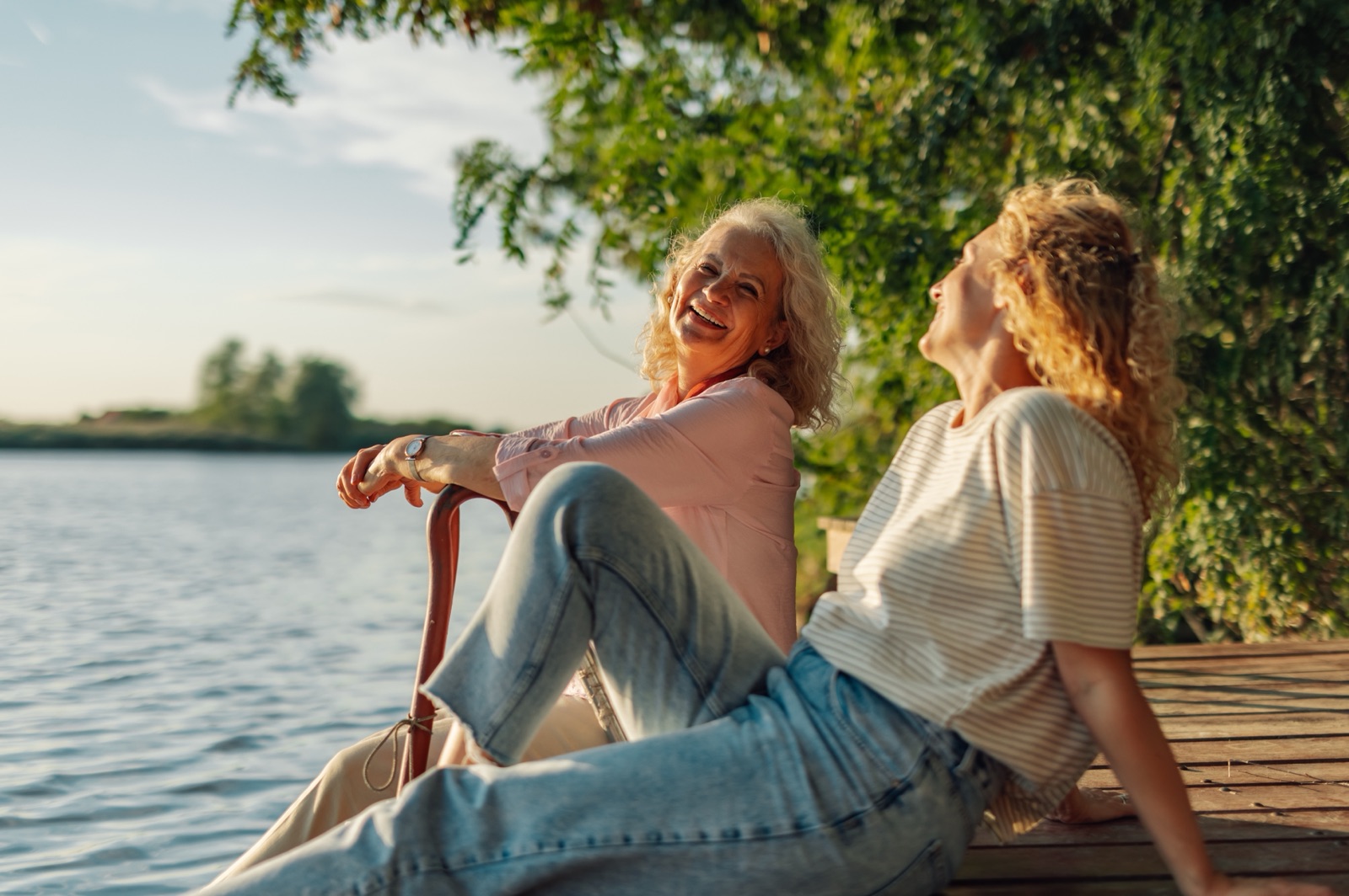 An older woman and a younger woman relaxing together beside a lake.