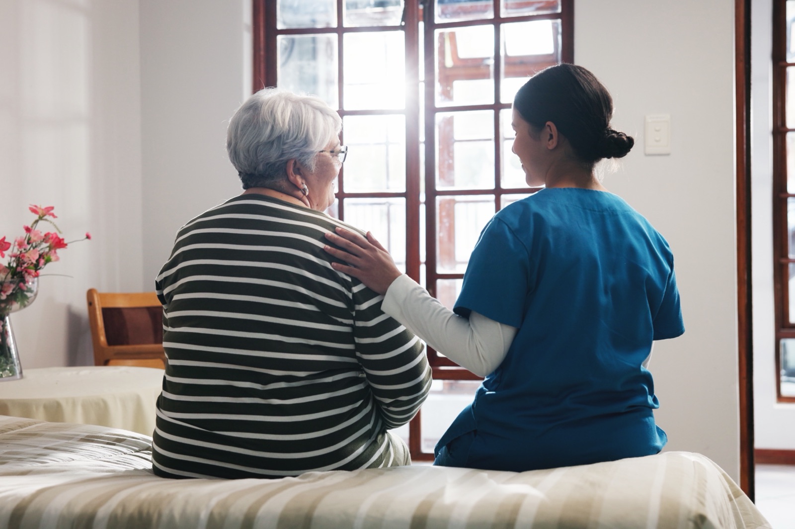 A care worker sitting beside an older woman with a hand resting on her shoulder.
