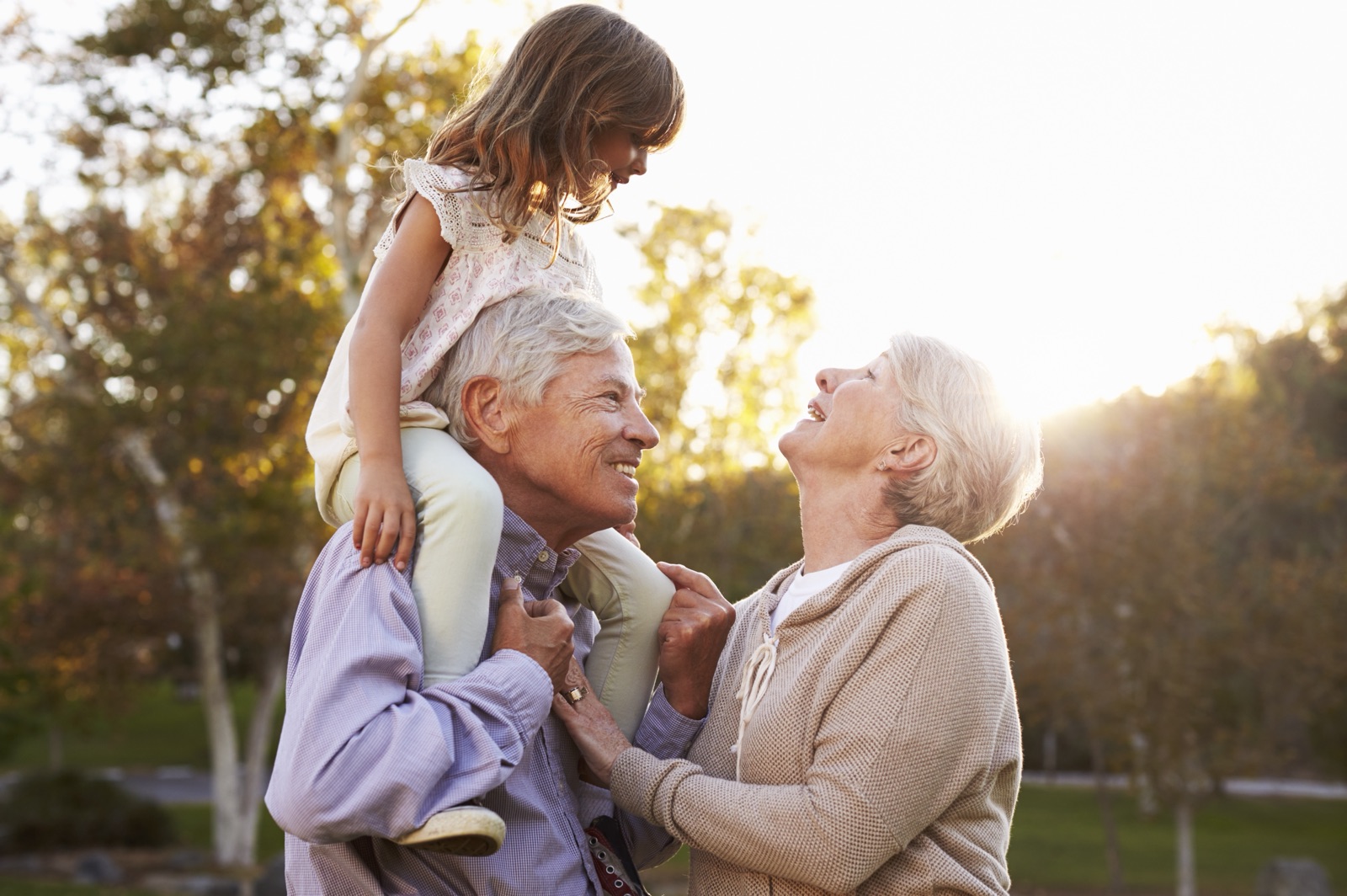 An older couple outdoors with a young girl sitting on the man’s shoulders.